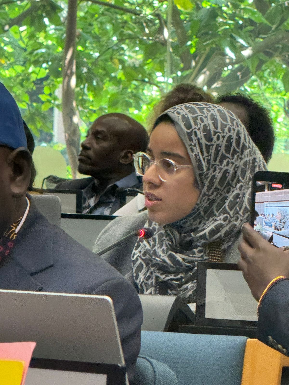 Oumnia wearing a patterned hijab and speaking into a microphone during a conference discussion